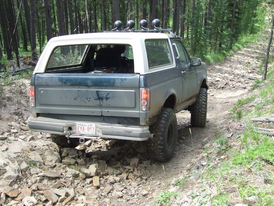 Ford Bronco on a rocky, wooded trail. License plate EYA-853