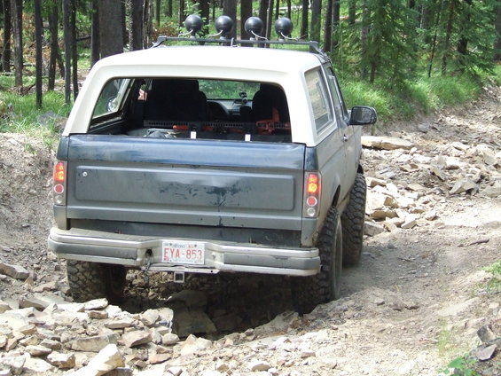 1990 Ford Bronco driving over rocks on a dirt trail, rear view