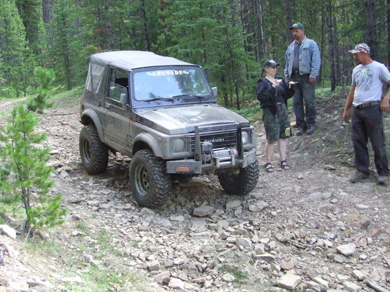 Suzuki Samurai with lifted suspension and winch on a rocky trail, three people standing nearby