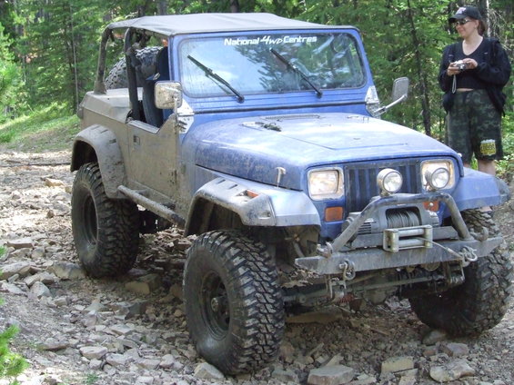 Blue Jeep Wrangler with a winch and off-road tires on a rocky trail