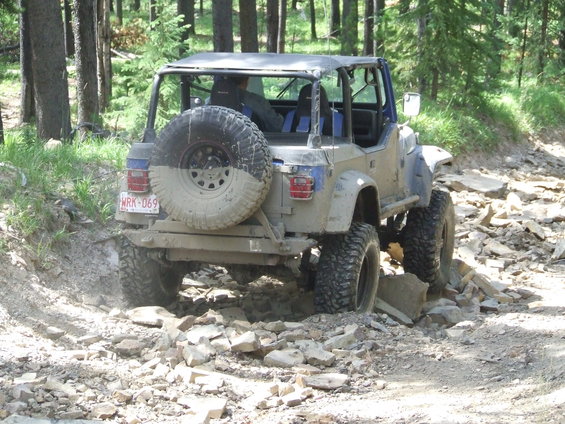Mud-splattered off-road vehicle with spare tire on back, navigating rocky terrain