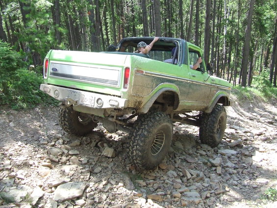 Green lifted Ford Bronco with removable top driving on a rocky forest trail