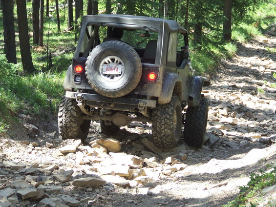 Jeep Wrangler driving on a very rocky trail through a forest