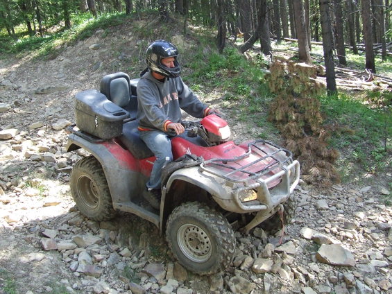 Red ATV with a rider on a rocky forest trail