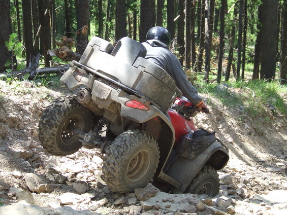 Red ATV with grey storage box navigating rocky terrain