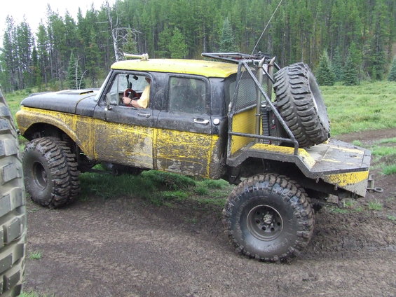 Modified pickup truck with large tires, spare tire mounted on rear, and roll cage