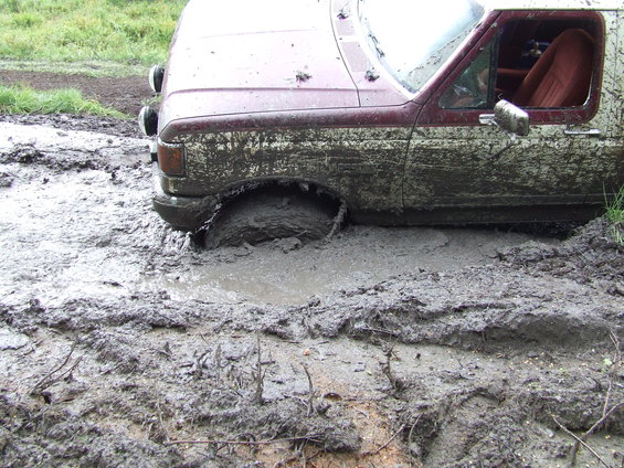 Maroon and white 1990 Ford Bronco stuck in deep mud, front wheel submerged