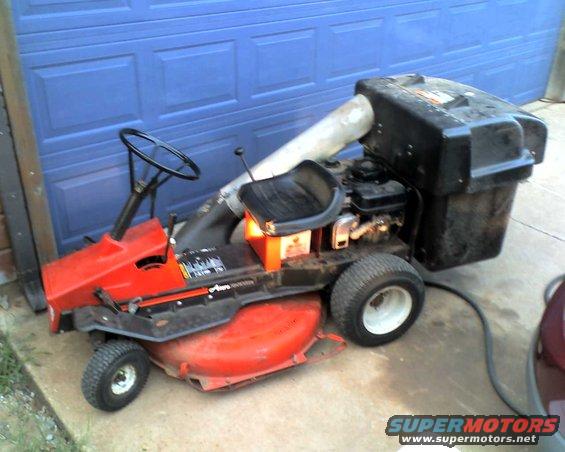 Riding lawn mower with a bagger attachment parked in front of a blue garage door