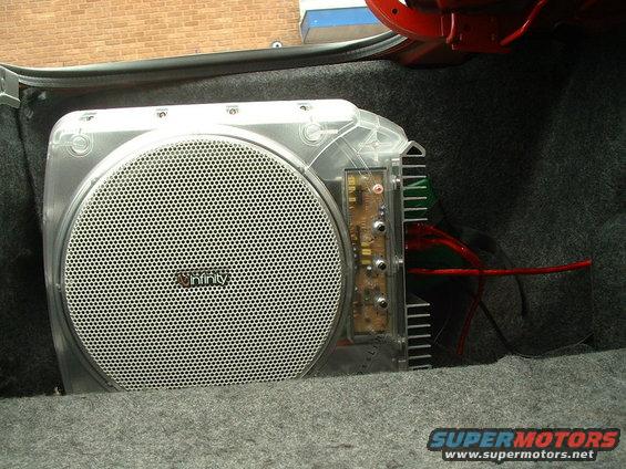 Car trunk with an Infinity subwoofer installed, showing clear casing and red wiring
