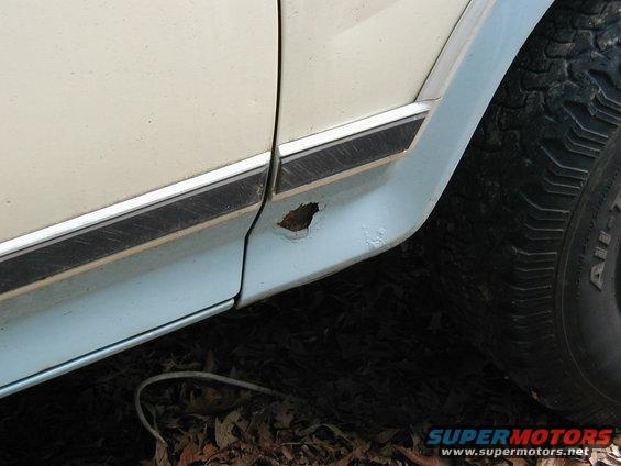 Close-up of a rusty lower door panel and tire on a light-colored vehicle