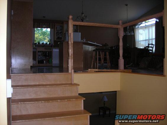 Stairs leading up to a living area with a kitchen visible in the background. A railing is under construction