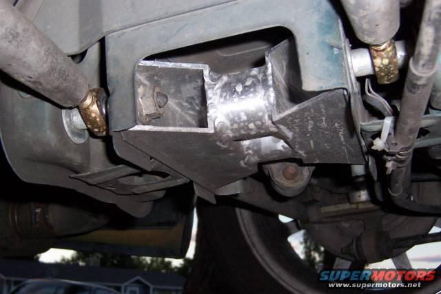 Custom metal bracket welded to vehicle frame with visible suspension components and exhaust pipe