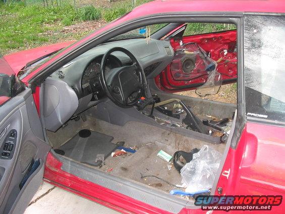 red car interior with doors open, dashboard, steering wheel, and floor are messy. Door panels removed