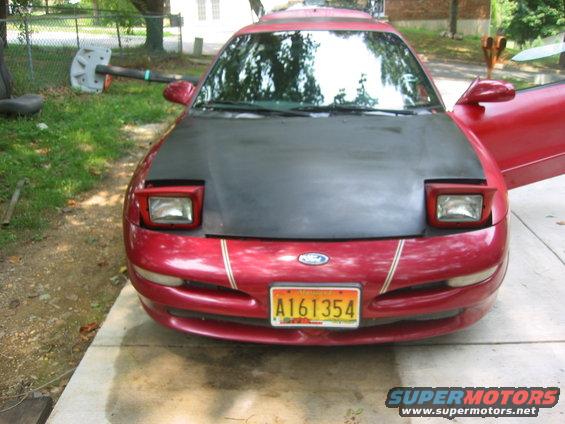 Red car with black hood, pop-up headlights, and a license plate reading A161354