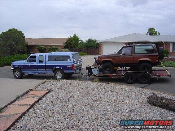 Brown Ford Bronco II on a trailer, towed by a blue Ford F-150 pickup truck