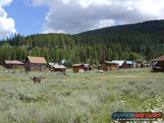 Rural village with wooden cabins and a dense forest on a hill under a cloudy sky