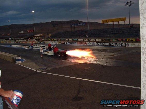 Jet dragster with flames shooting out the back on a race track at dusk