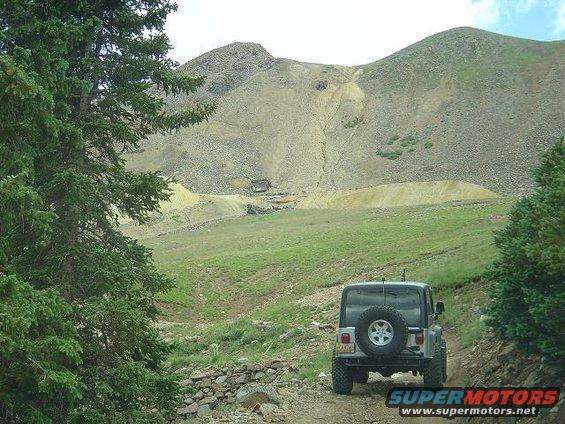 Silver Jeep Wrangler with spare tire on rear door, parked on dirt road