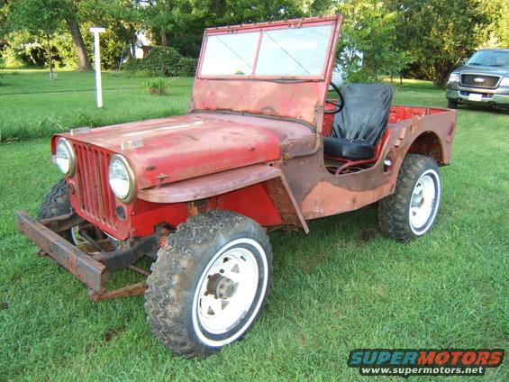 Red Willys Jeep with white-wall tires and rusty body panels, viewed from a 3/4 front angle