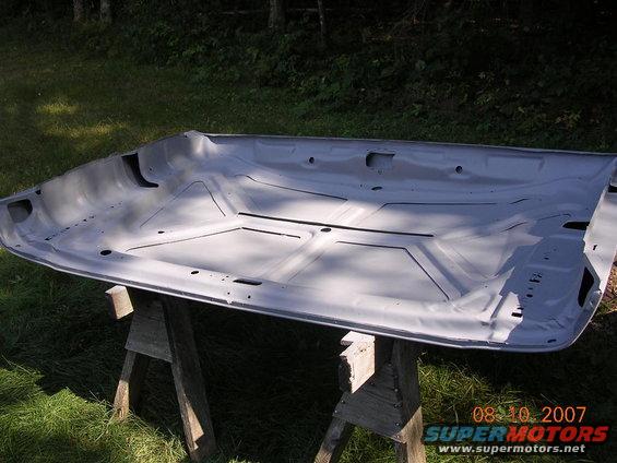 Underside of a car hood, painted gray, resting on two wooden sawhorses outdoors