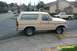 1985 Ford Bronco - A tan Ford Bronco is parked on the side of the road with a pickup truck in the background.
