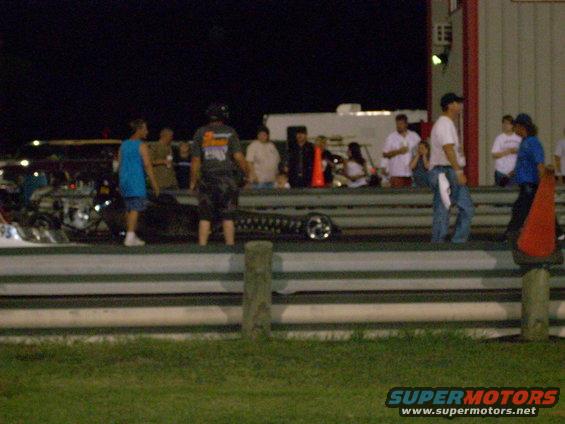 People gathered at a drag strip at night, with a race car visible on the track