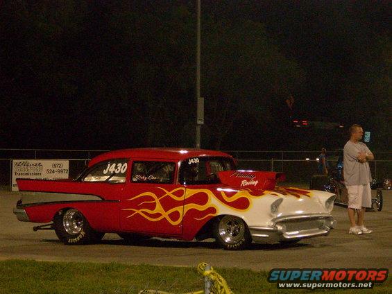 red and white drag car with flames, scoop on hood, man standing nearby