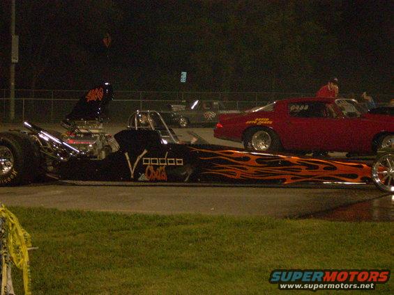 Dragster with flames and 'Voodoo Child' text, next to a red muscle car with racing decals