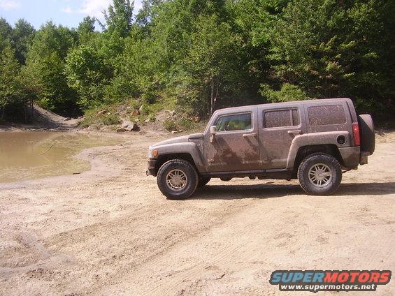 Mud-covered Hummer H3 parked on a dirt track next to a muddy puddle