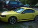 2003 Ford Mustang - A yellow 2003 Ford Mustang is parked outside, with a blue Ford Bronco and other vehicles in the background.