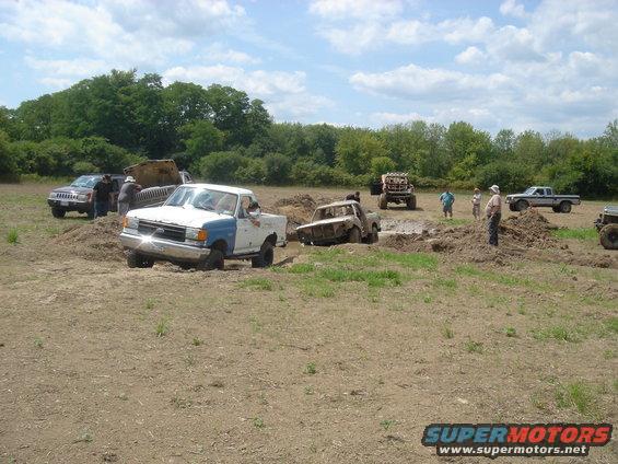 White and blue pickup truck stuck in mud pit, front 3/4 view. Likely 1987-1991 model