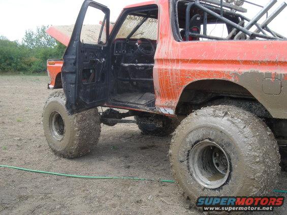Mud-covered 1979 Ford F-250 with open door and hood, modified for off-road use