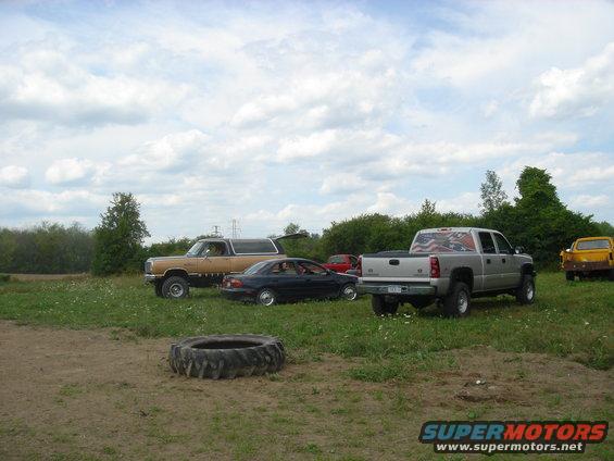tan SUV, black car, silver pickup with flag decal, and yellow vehicle parked in a field