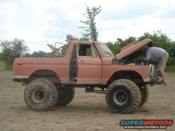 Orange Ford Bronco with lifted suspension and large tires, hood up, person working on engine