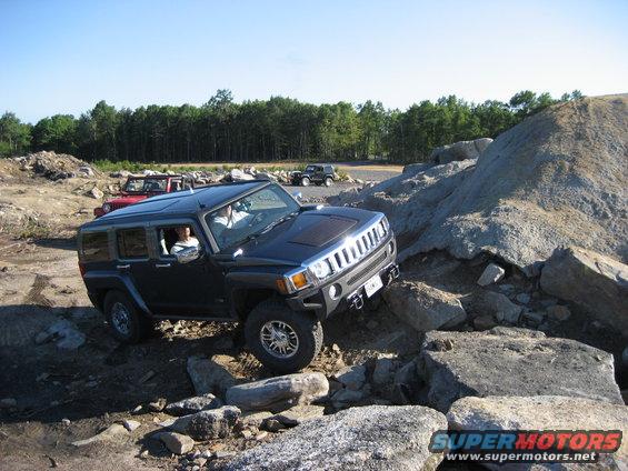 Dark gray Hummer H3 navigating rocky terrain, front-left wheel elevated