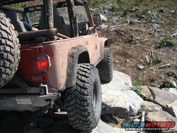 2003 Jeep Wrangler on rocks, rear view. Muddy body, large off-road tires