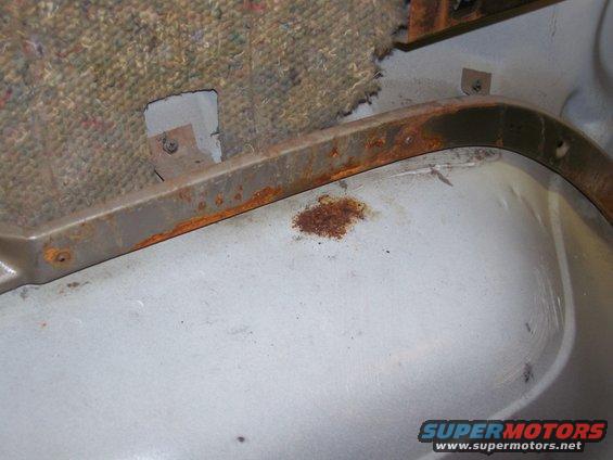 rusted metal trim above light gray floor panel with torn carpet backing