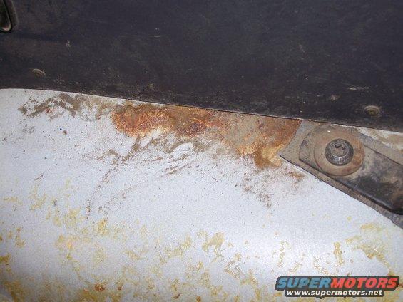 rusted metal panel with a bolt and bracket, part of a vehicle's interior