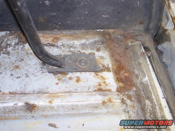 Rusted floor pan with a bent metal bracket and bolt