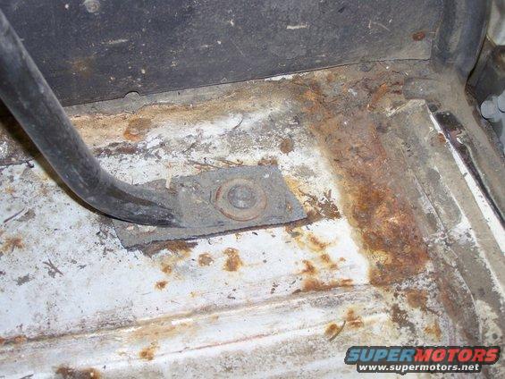 rusted floor pan with a metal bracket and bolt visible