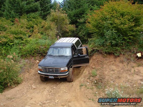 1996 Ford Bronco with camper shell driving on a steep dirt trail, driver's door open