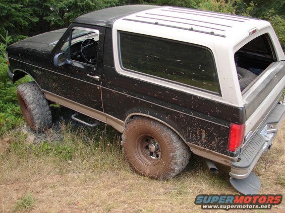 Black and white Ford Bronco on a dirt trail, tires covered in mud