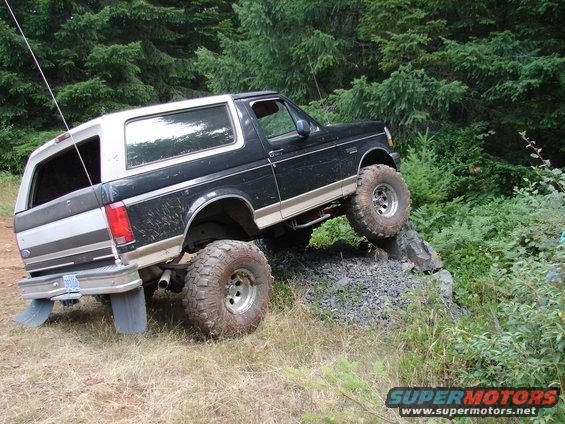 1996 Ford Bronco with lifted suspension and off-road tires climbing a rock obstacle