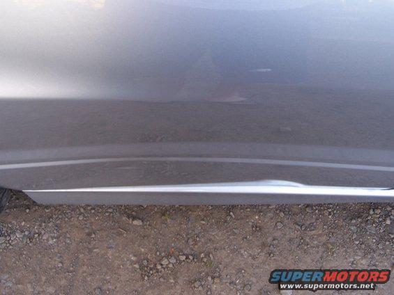 Close-up of a gray car door showing a dent and a chrome trim piece