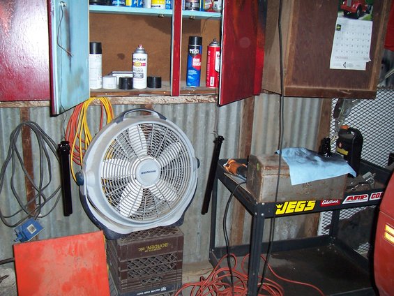 Garage interior with a large fan, tool cart, shelves with spray cans, and a calendar on the wall