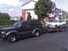 1989 BMW 3 Series - A dark-colored SUV is towing a white coupe on a flatbed trailer down a street with apartment buildings in the background.