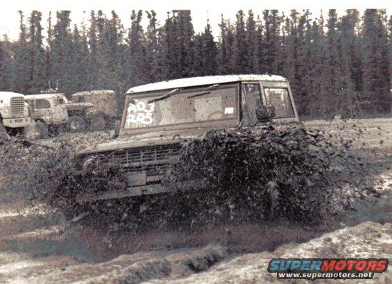 1971 Ford Bronco driving through mud, splashing dirt. White text on windshield
