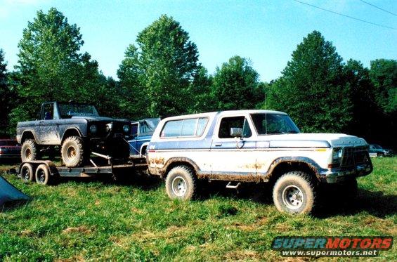 White and blue 1978 Ford Bronco on trailer towed by another Bronco, muddy