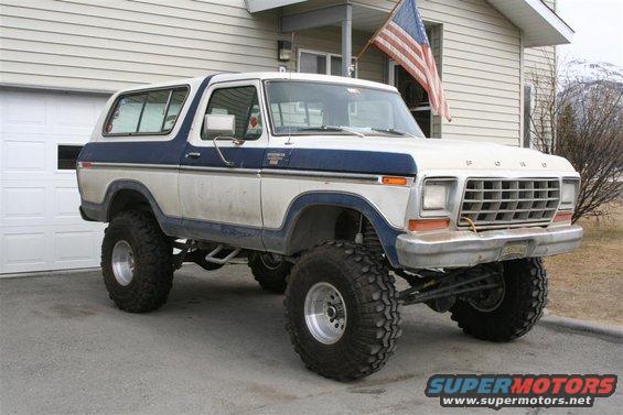 White and blue 1978 Ford Bronco with lifted suspension and large tires parked in front of a garage
