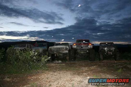 Four lifted trucks parked outdoors at dusk